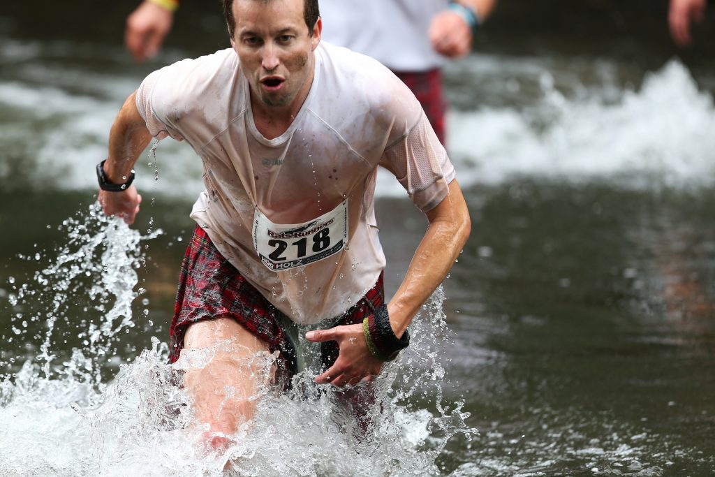 Man running through water in a race. Massive action an important ingredient to growth